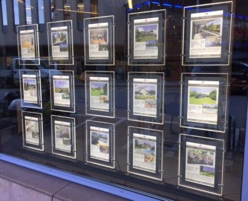 Système d'affichage lumineux suspendu sur câbles, idéal pour agences immobilières et de voyages, disponible en plusieurs formats et orientations, avec rétroéclairage LED garanti 60,000 heures, en vente chez C.Diff Prom, livraison rapide en Suisse.